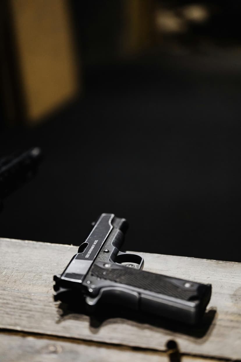 Colt 1911 semi-automatic pistol with textured grips resting on light-colored weathered wood grain planks.