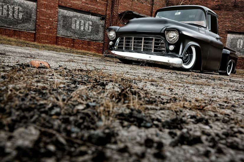 Matte black custom classic truck with chrome grille and whitewall tires parked against a brick wall.