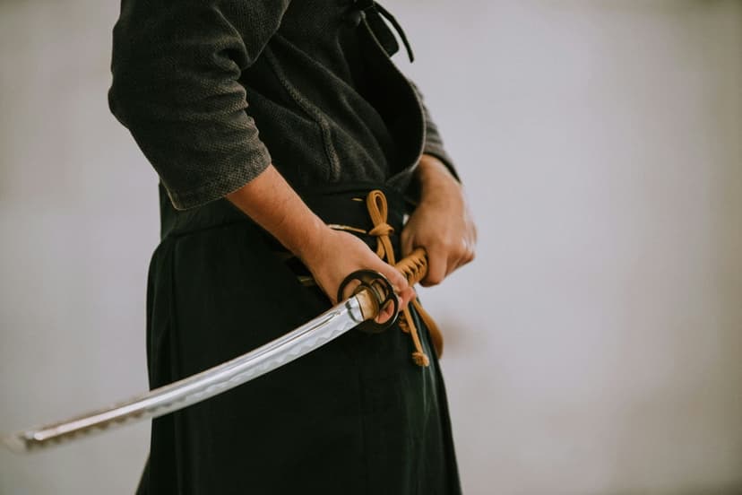 Samurai warrior hands firmly gripping a detailed katana hilt and blade against a neutral textured background.