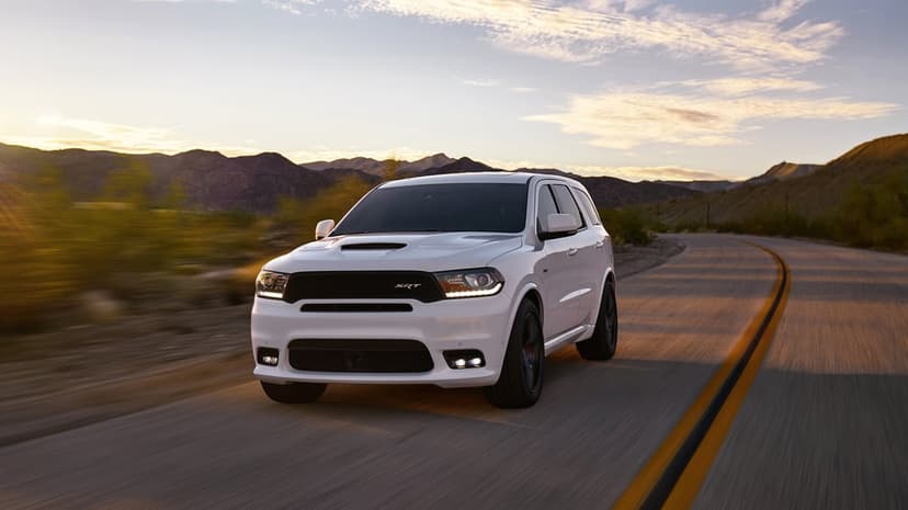 White Dodge Durango SRT SUV driving on a winding desert road during golden hour with mountains in the background.
