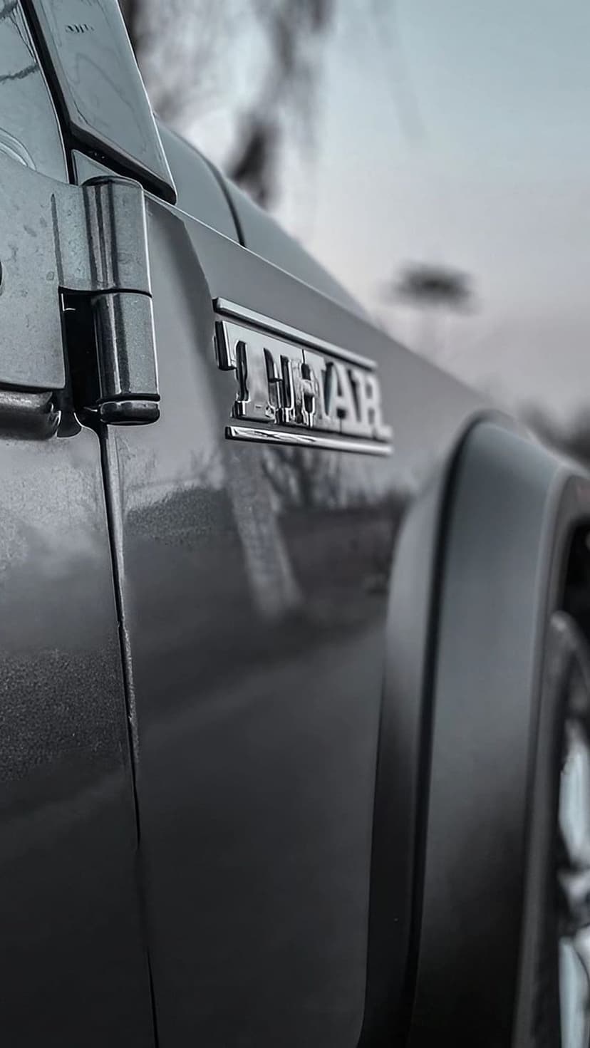 Chrome Thar emblem and a black door hinge on a vehicle side with a soft-focus outdoor background.