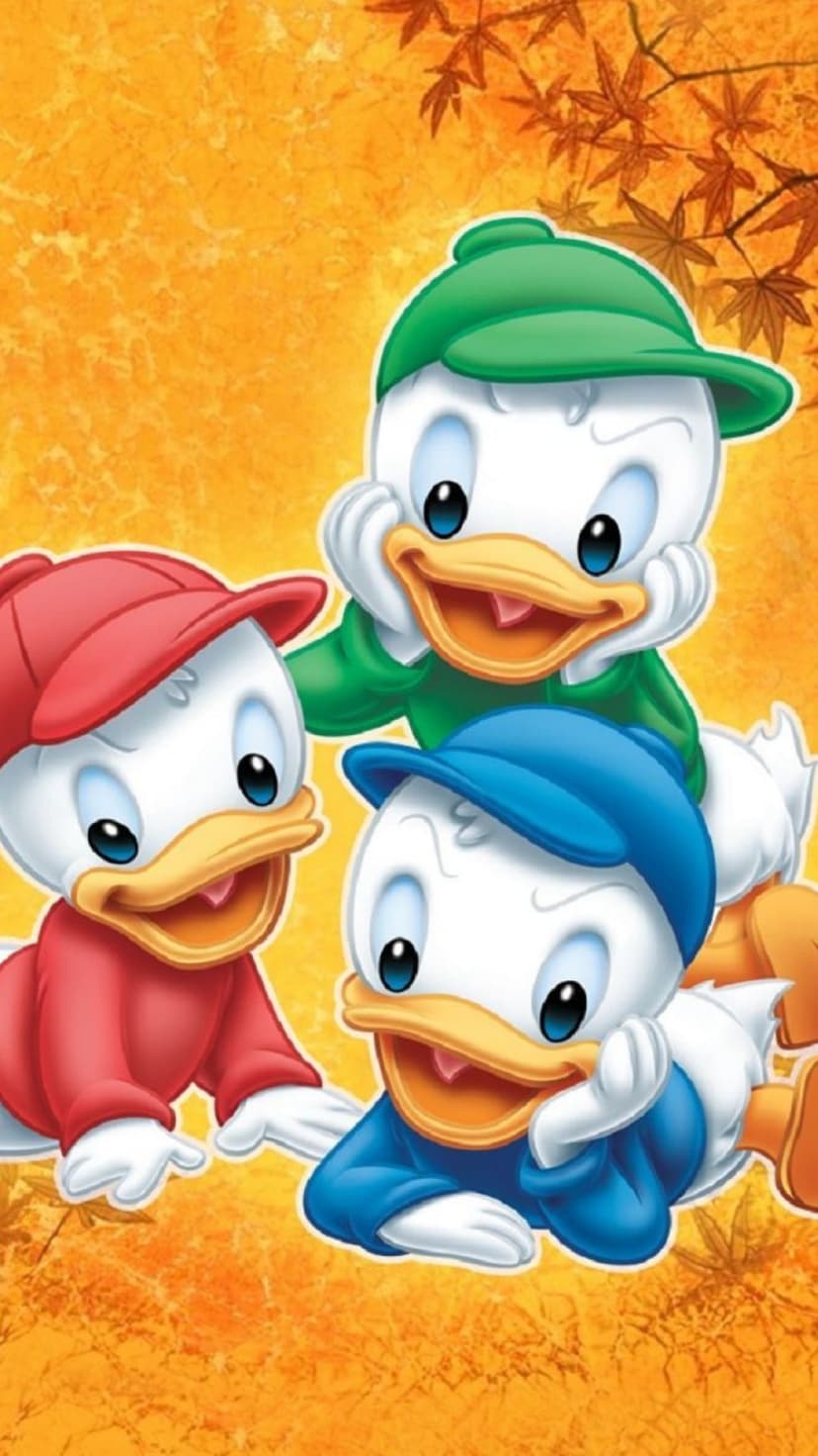 Three ducklings in red, green, and blue caps lean on their hands against an orange autumn leaf background.