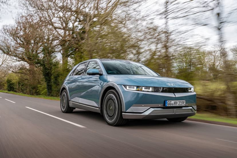 Blue Hyundai Ioniq 5 electric car driving on a rural road with motion blur and forest background.
