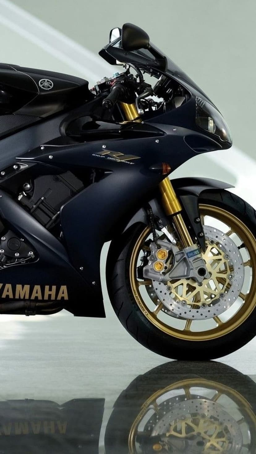 Yamaha R1 motorcycle with dark blue fairing, gold front forks, and gold alloy wheels reflected on a glossy floor.