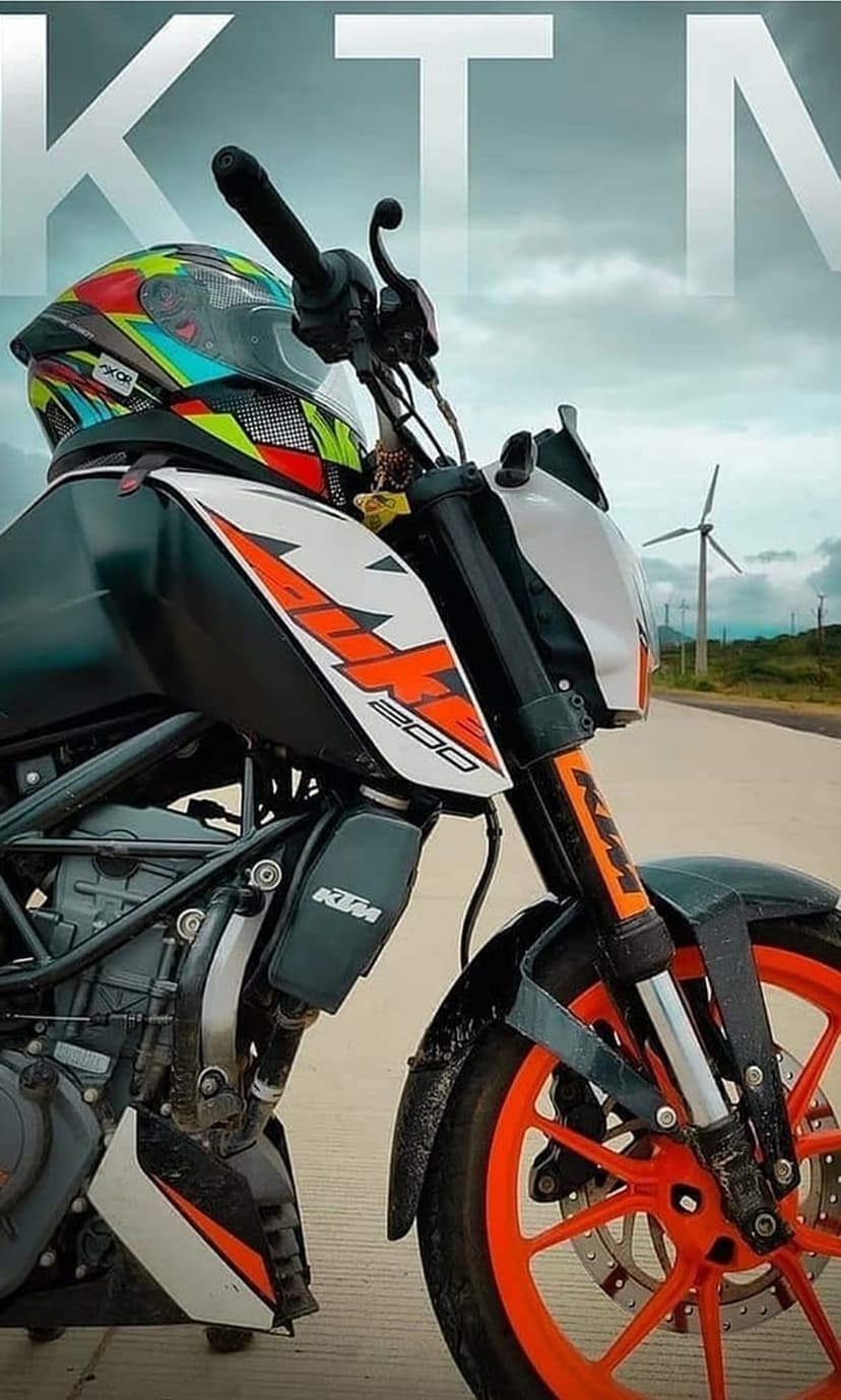 KTM 200 motorcycle with an orange frame and a colorful helmet on its seat against a backdrop of wind turbines.