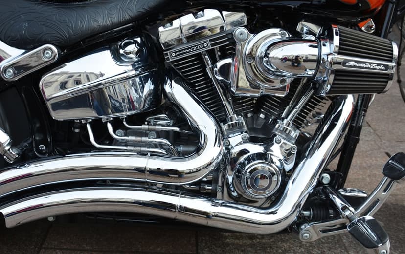 V-twin motorcycle engine with reflective chrome exhaust pipes and a circular air intake in a detailed close-up.