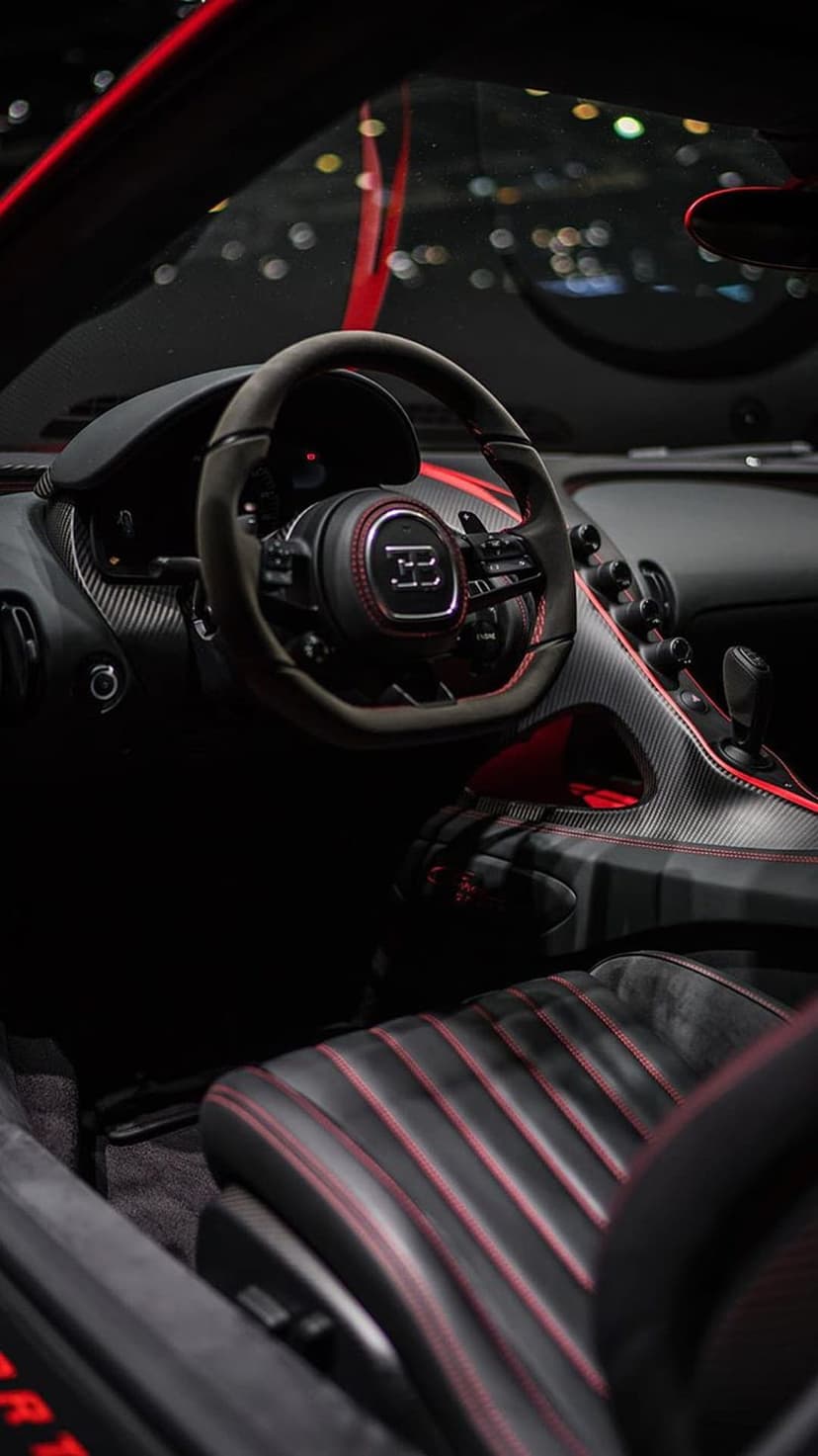 Bugatti steering wheel with a silver EB logo, red stitching on black leather, and carbon fiber dash details.