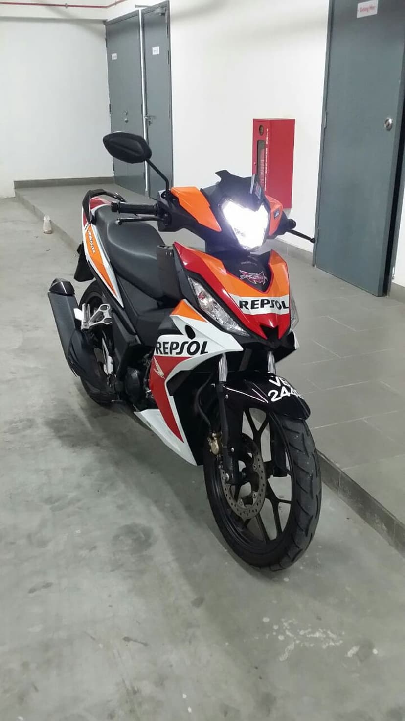 Honda RS-X Repsol motorcycle with orange and white racing livery parked on a concrete floor in a garage.