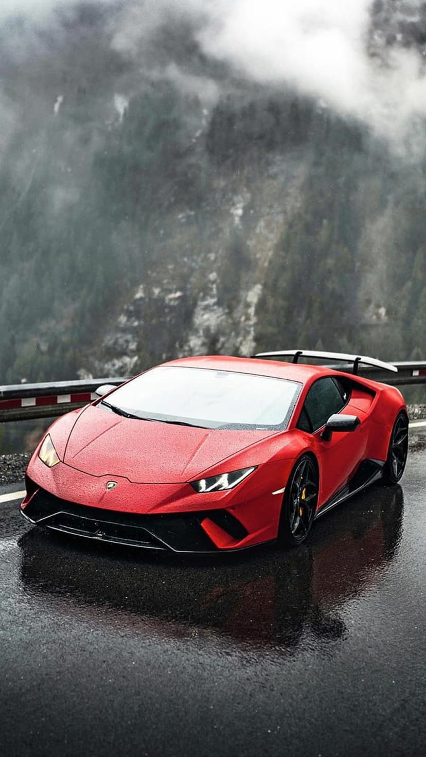 Red sports car parked on a wet mountain road with dense fog and evergreen trees visible in the background.