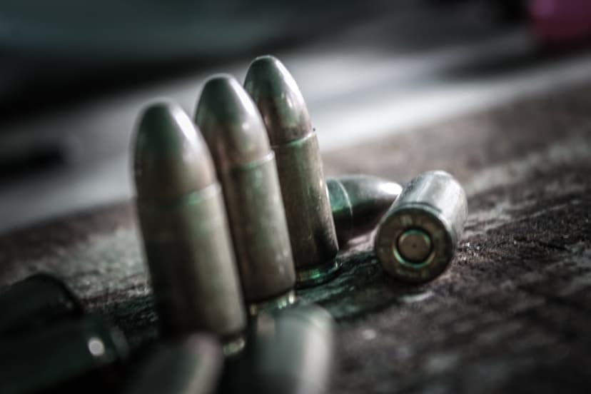 Brass ammunition rounds resting on a dark, textured surface with shallow depth of field and dramatic side lighting.