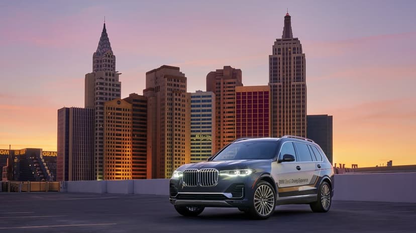 Dark BMW X7 SUV with headlights on a rooftop against a New York-style city skyline at purple dusk.