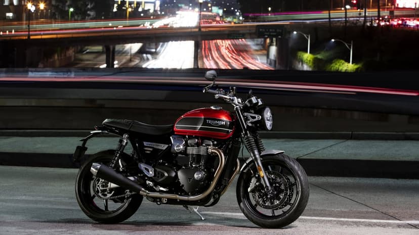 Red Triumph Speed Twin motorcycle parked at night with long exposure light trails on an urban highway bridge.