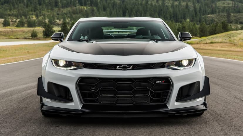 Front view of a white Chevrolet Camaro ZL1 1LE with black aero parts on a paved race track with forest background.