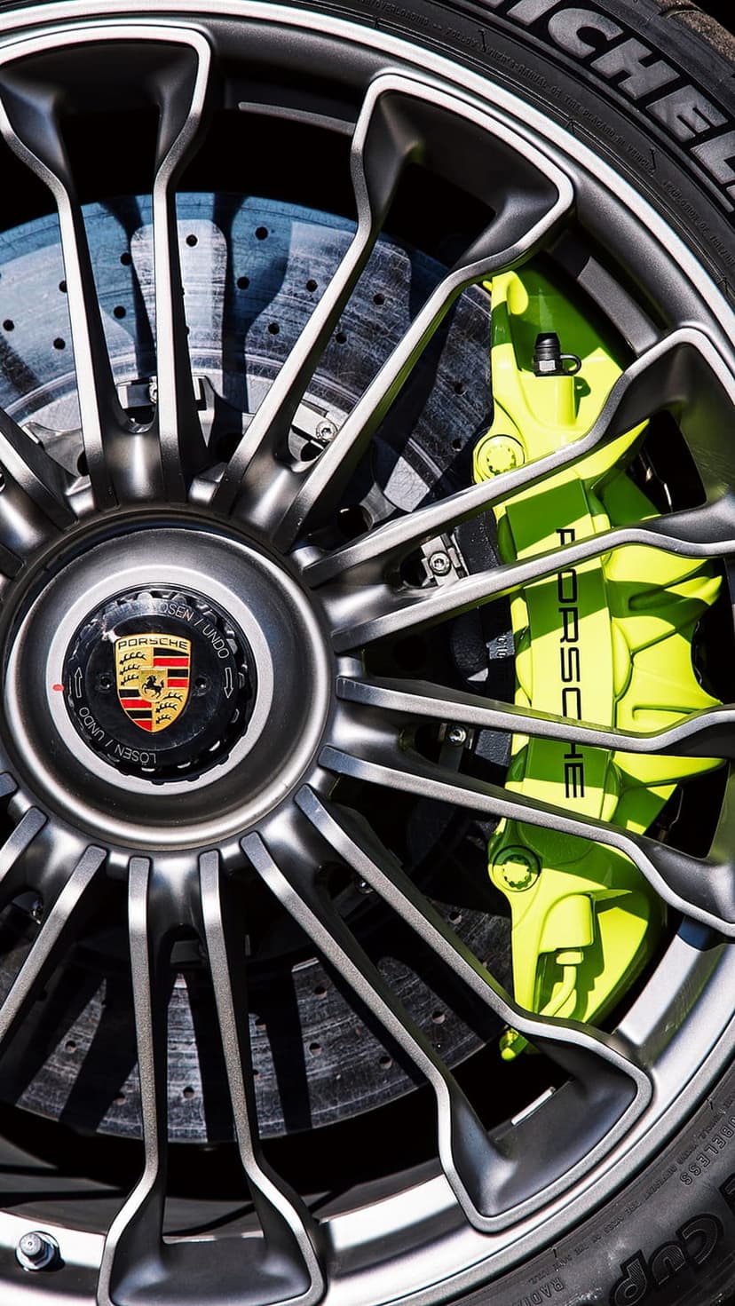 Neon green Porsche brake caliper behind a dark multi-spoke alloy wheel with a central crest on a Michelin tire.