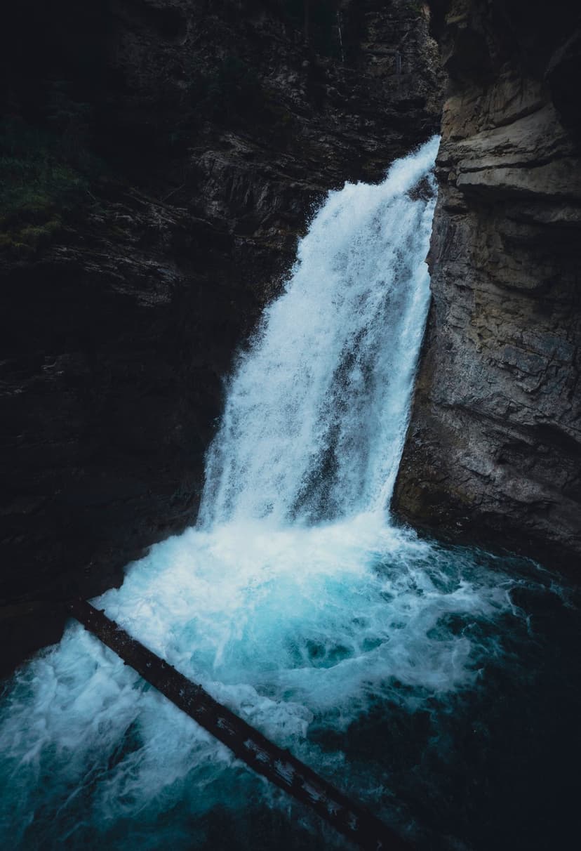 Powerful waterfall flows into a turquoise pool surrounded by dark canyon walls and a submerged fallen log.