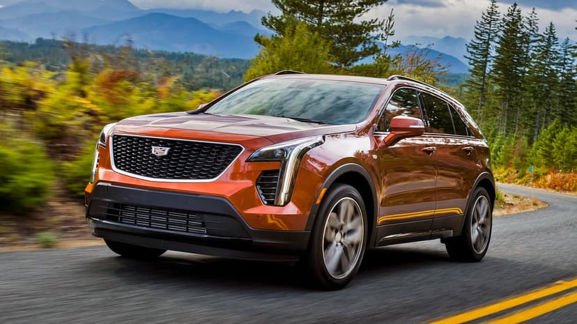 Burnt orange Cadillac XT4 SUV driving on a winding road with motion blur and mountain scenery background.