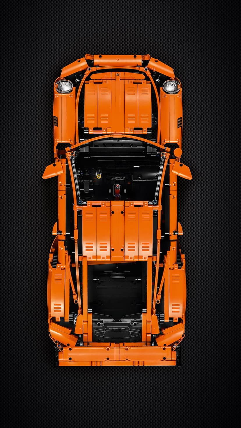 Orange Lego Technic supercar shown from a top-down view resting on a black carbon fiber textured background surface.