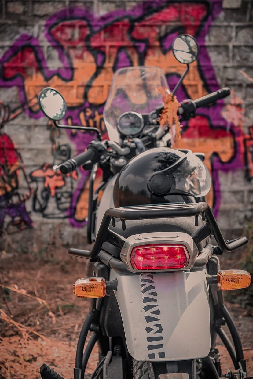 White motorcycle with a black helmet parked against a vibrant purple and orange graffiti-covered brick wall.
