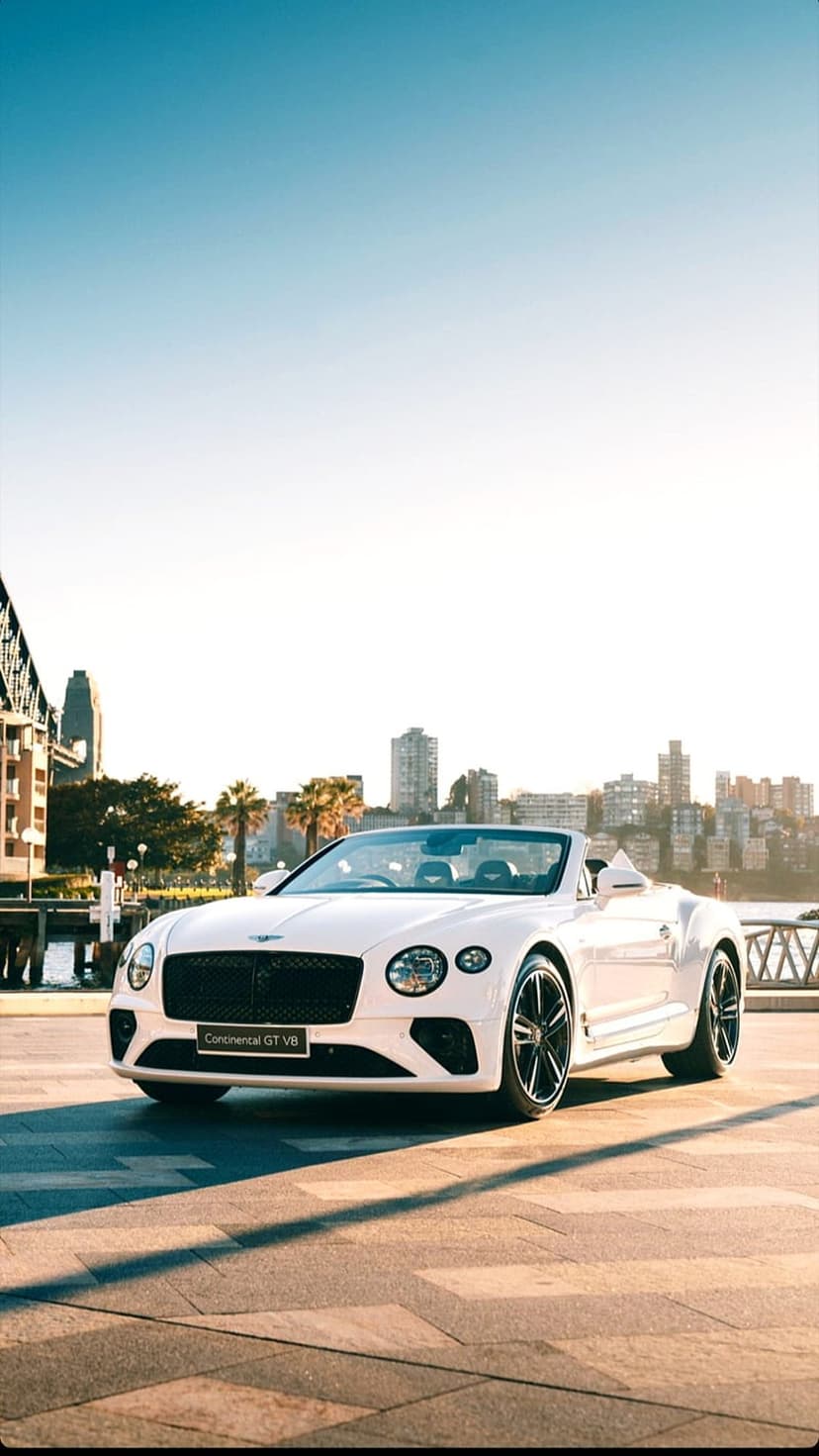 White Bentley Continental GT convertible parked in Sydney with the Harbour Bridge and palm trees background.