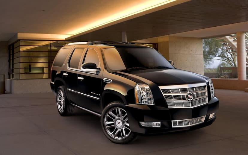 Black Cadillac Escalade Hybrid with chrome wheels parked in a modern concrete garage under warm sunset light.