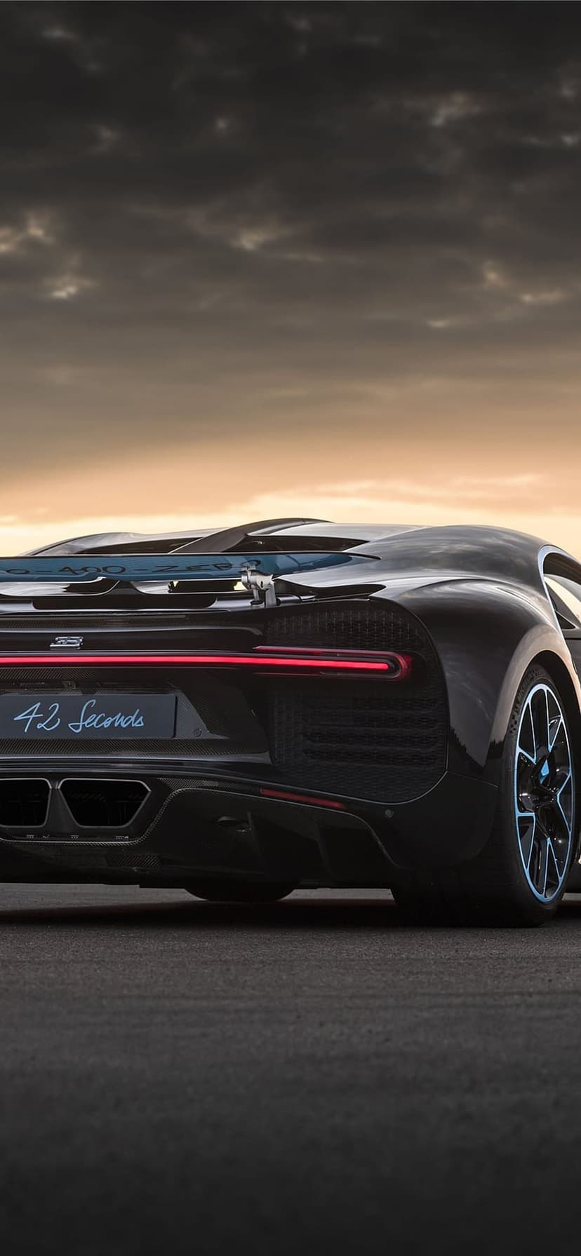 Black Bugatti Chiron rear view with a horizontal red taillight bar and 42 Seconds badge on a tarmac at sunset.