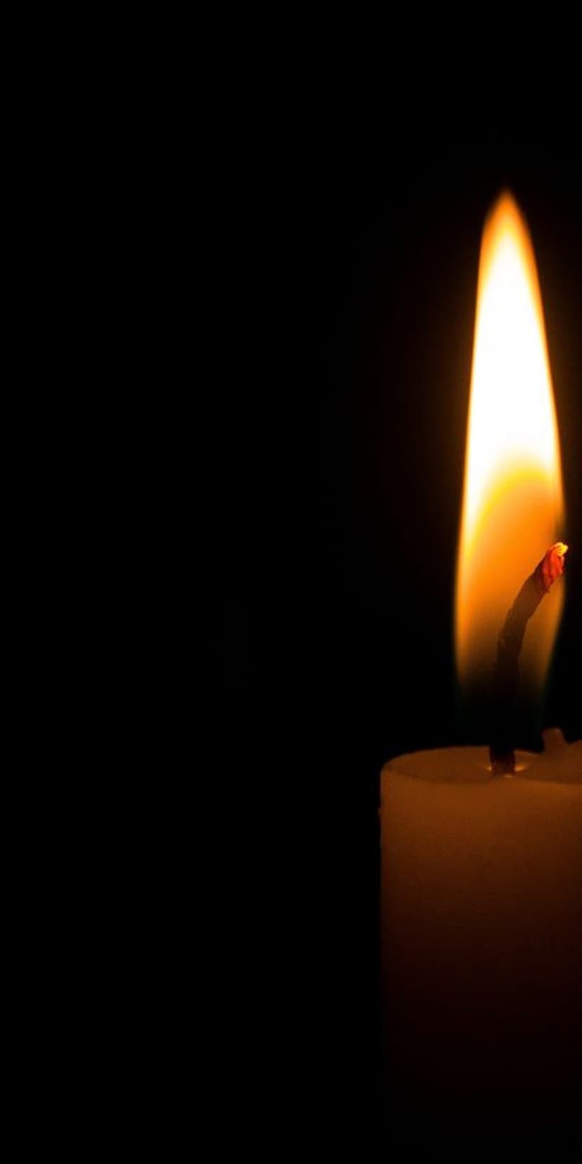 Solitary yellow candle flame with a glowing orange core stands centered against a solid black background.