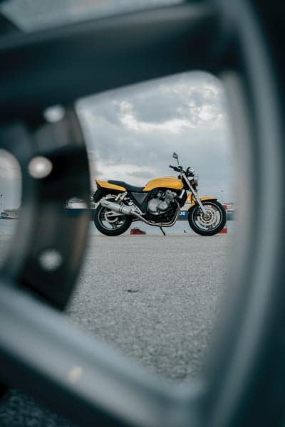 Yellow Motorcycle Reflected in Car Wheel Rim
