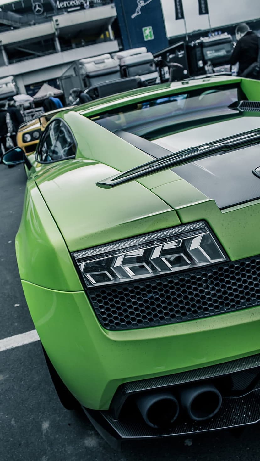 Lamborghini Aventador rear with green paint, Y-shaped LED taillights, and carbon fiber exhaust on a racetrack.