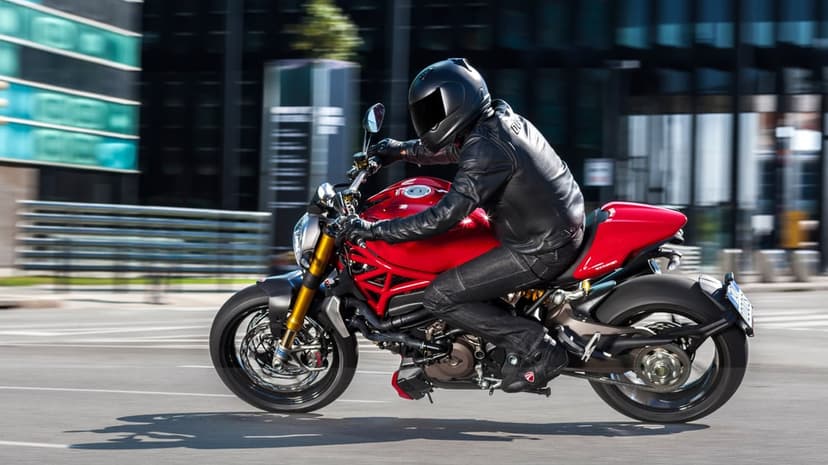 Red Ducati motorcycle with rider in black leather gear riding on a blurred city street in daylight.