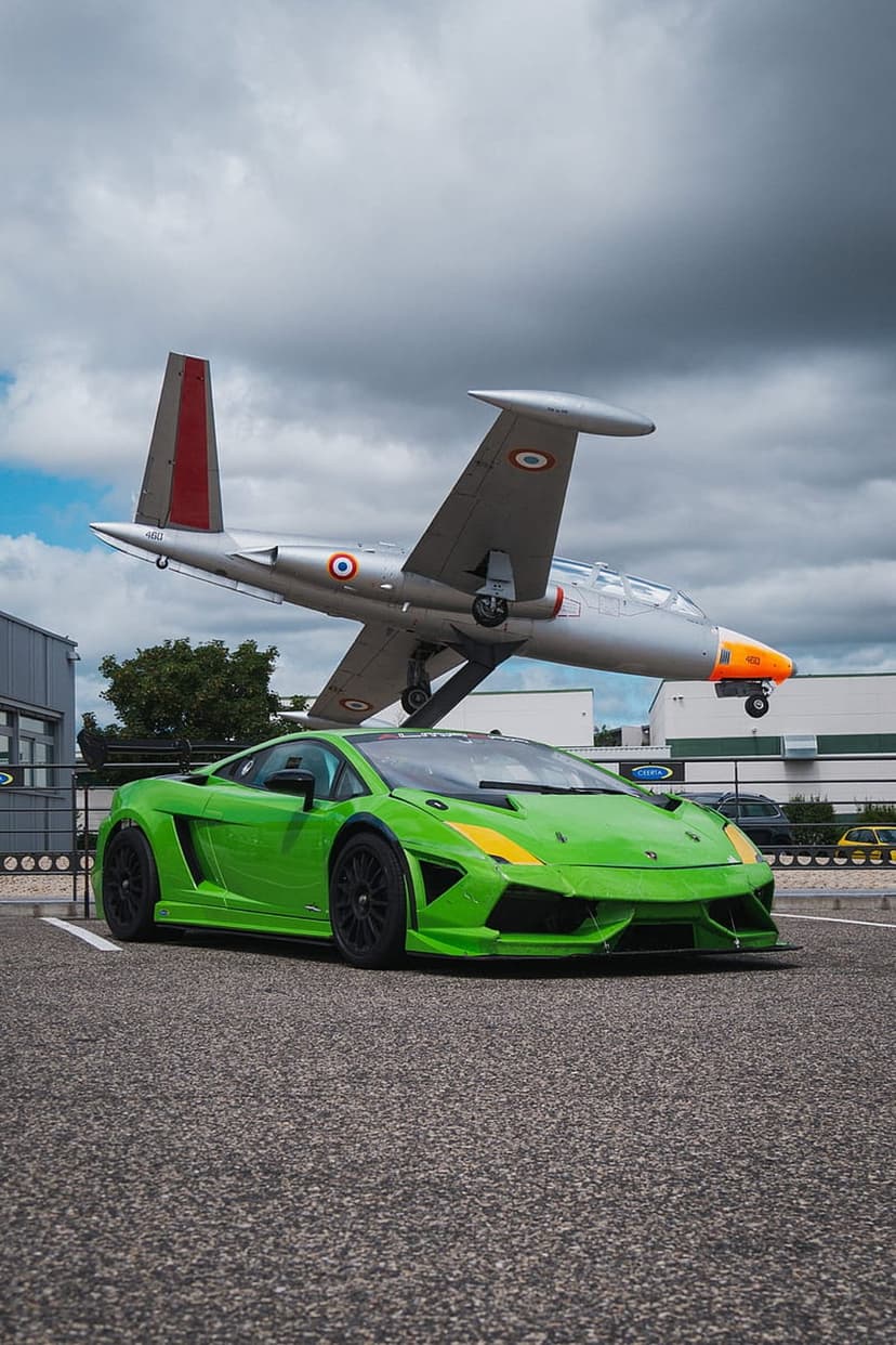 Green Lamborghini parked on an airfield runway in front of a silver jet plane under a moody, overcast sky.