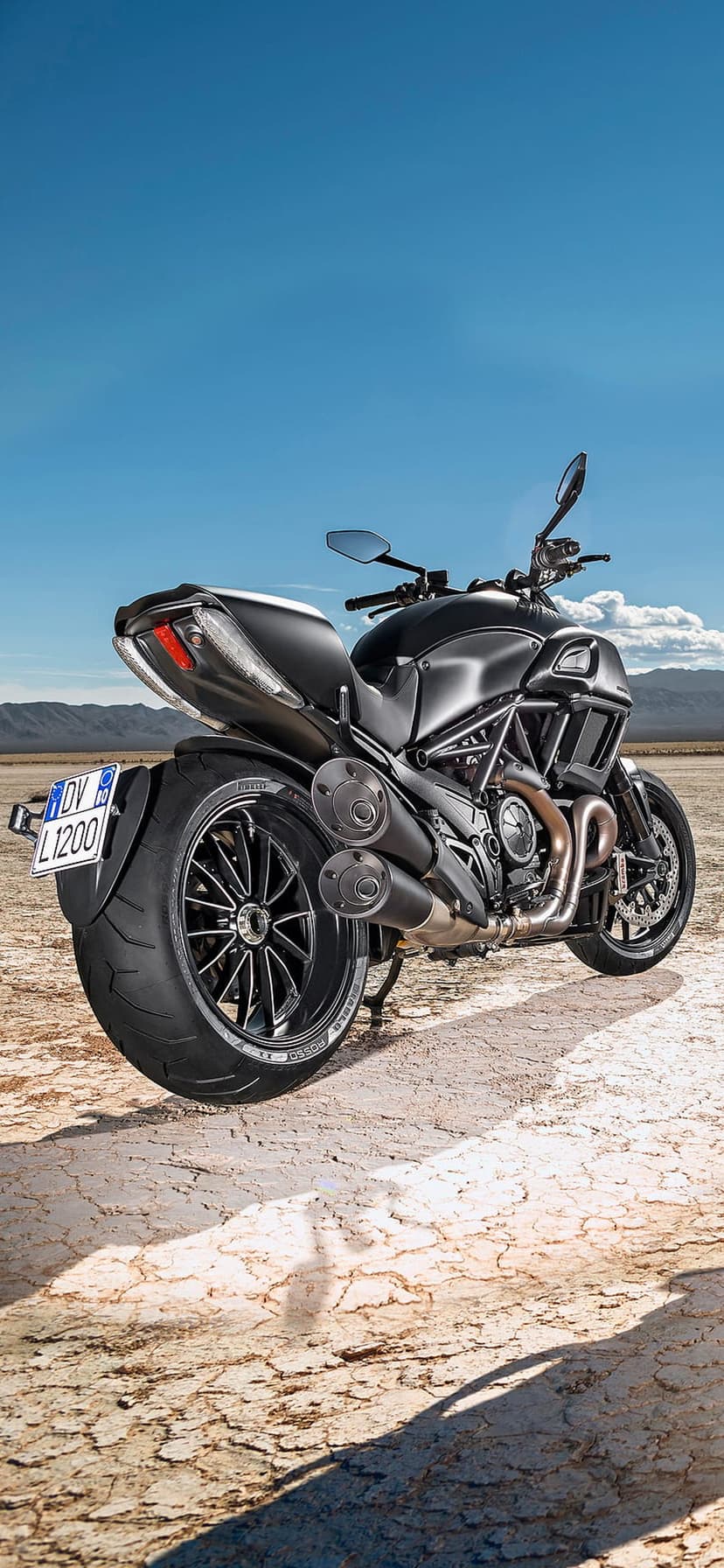 Ducati Diavel 1200 motorcycle parked on cracked desert earth under a clear blue sky with distant mountains.