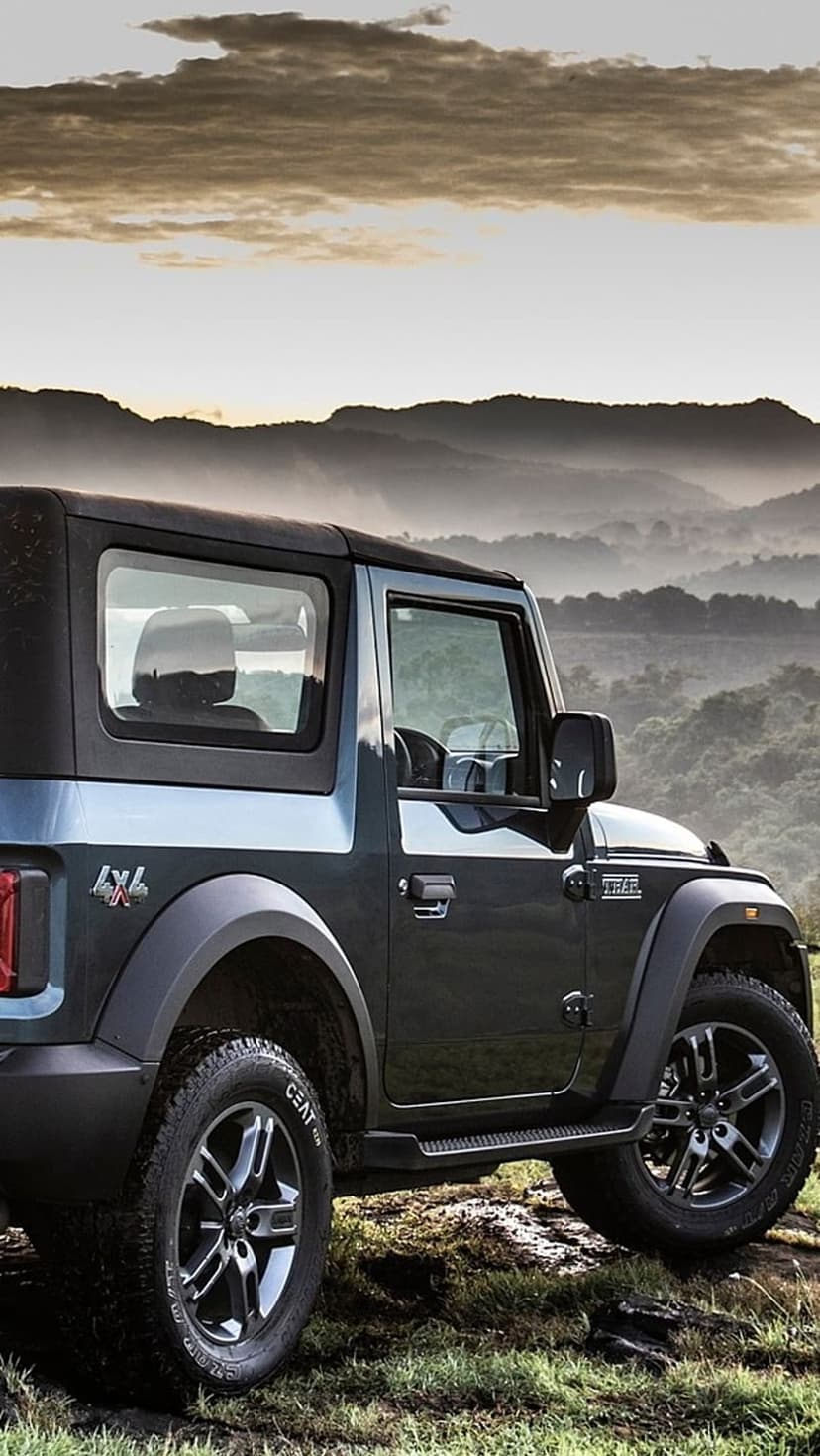 Mahindra Thar SUV parked on a grassy mountain cliff surrounded by thick morning mist and gray clouds.