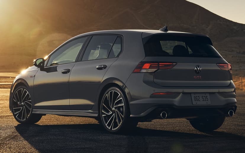 Rear view of a grey Volkswagen Golf GTI hatchback parked on asphalt during golden hour with mountains.