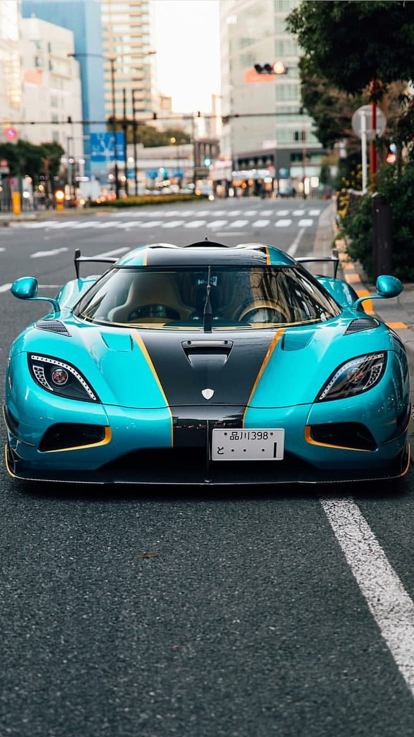 Koenigsegg Agera RS in bright blue with gold accents parked on a city street during the day from a low perspective.