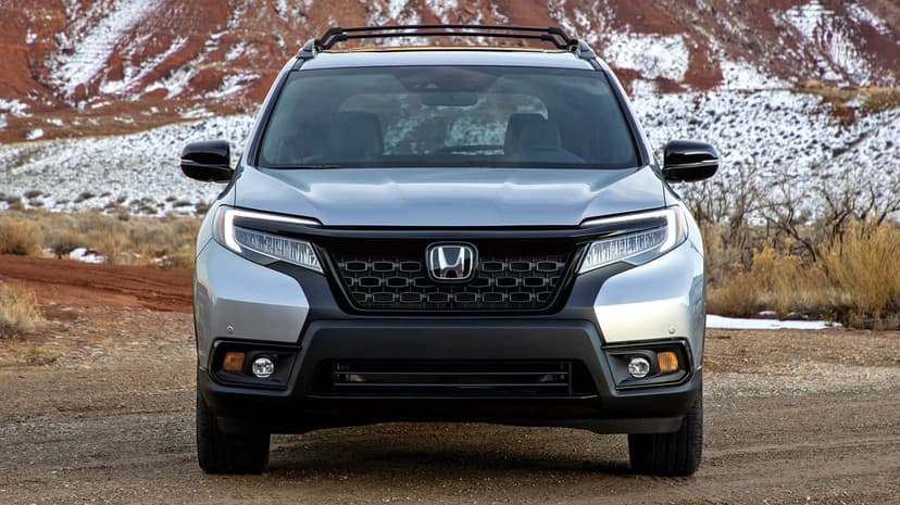 Silver Honda SUV front view on a dirt path with red rock mountains and snow in the background under soft light.