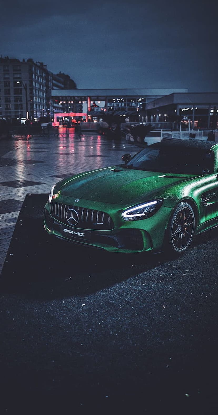 Emerald green Mercedes-AMG GT S parked on a wet asphalt street under dark city lights with vibrant reflections.