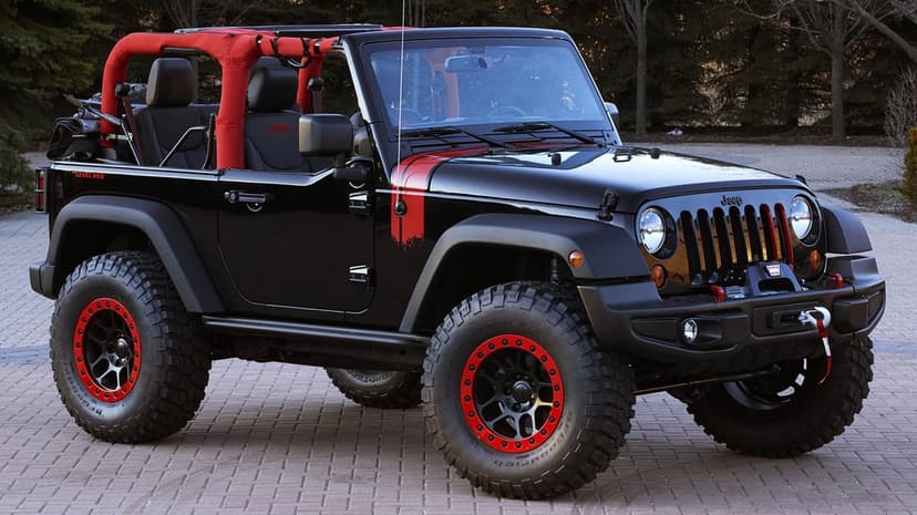 Modified black Jeep Wrangler with red accents and mud tires parked on a stone walkway in natural light.