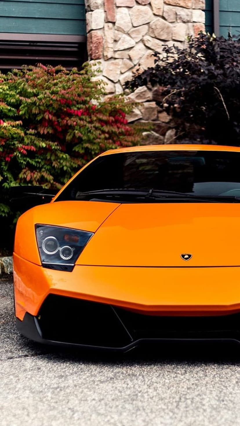 Orange Lamborghini Aventador front end featuring sleek headlights positioned near a weathered stone wall outside.