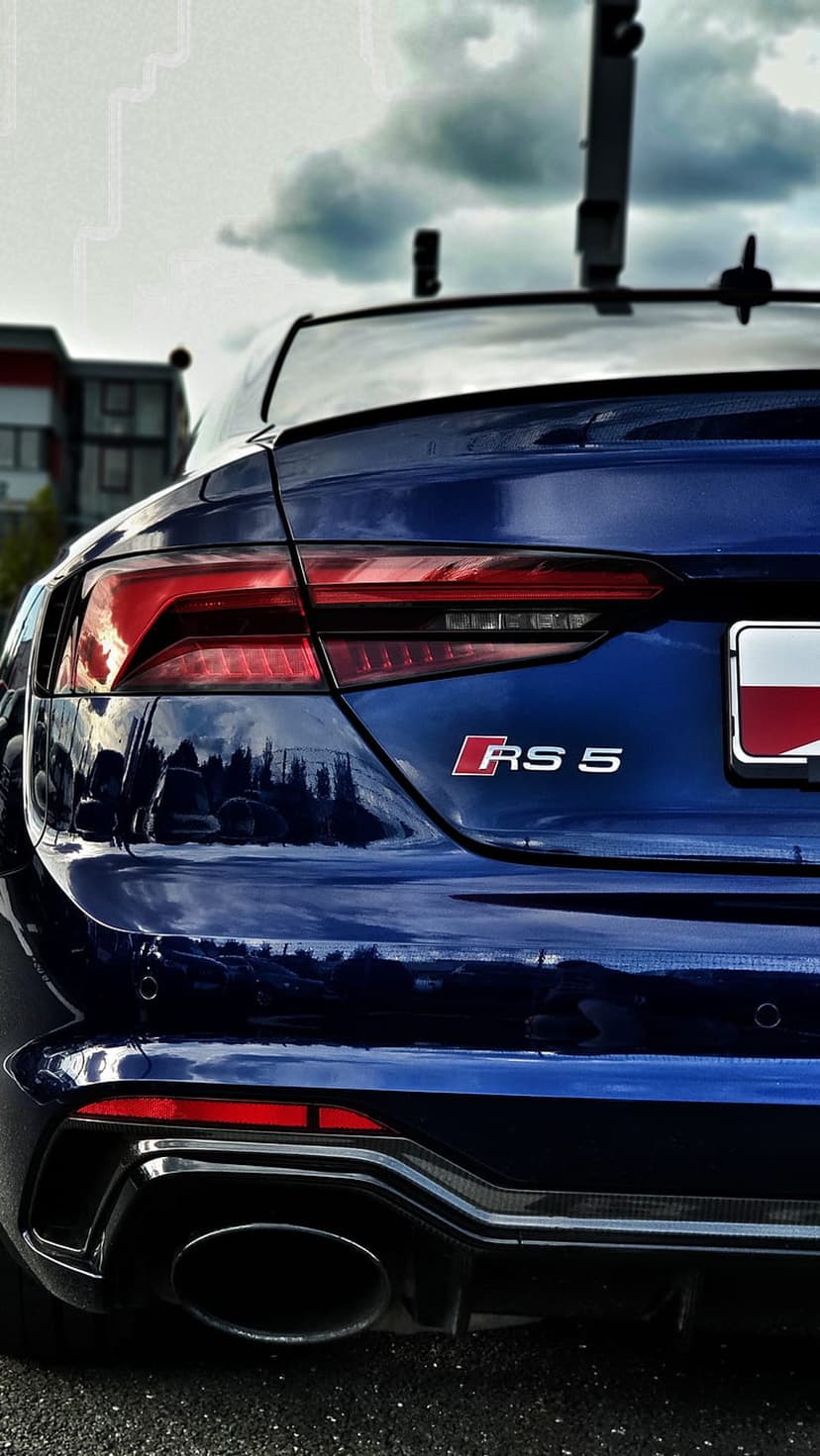 Blue Audi RS 5 rear view showing sharp LED taillights, a chrome badge, and an oval exhaust under a cloudy sky.