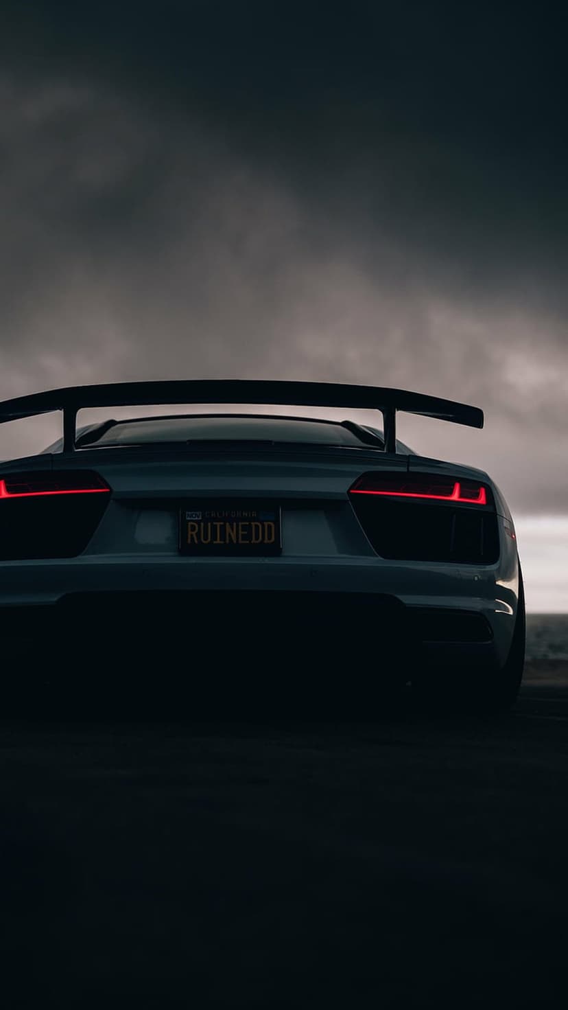 Audi R8 rear exterior featuring red LED taillights and a RUINEDD plate beneath a dark, moody overcast sky.