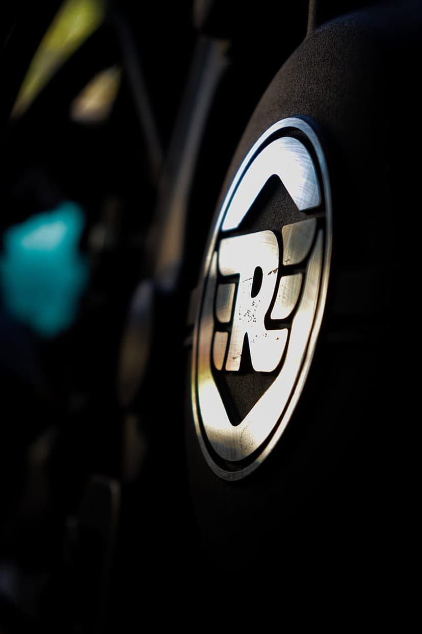 Royal Enfield silver winged logo on a dark textured motorcycle surface with a blurred black background.