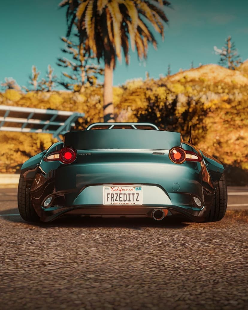 Rear view of a widebody teal Mazda MX-5 parked on a road with palm trees and a sunny sky in the background.