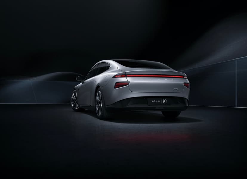 Rear view of a silver XPeng P7 electric car with glowing red tail lights in a dark minimalist studio.
