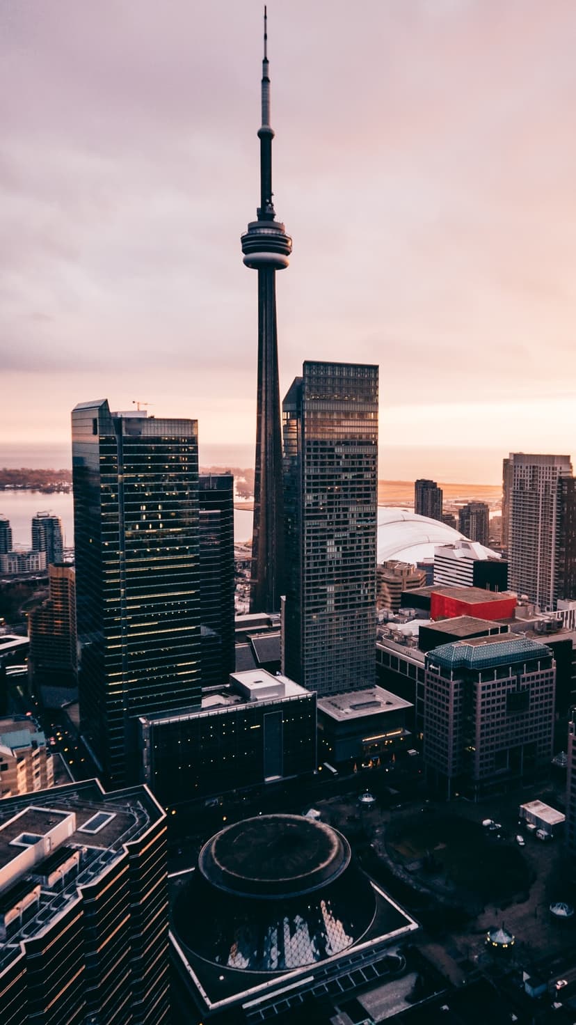 CN Tower stands tall above illuminated Toronto skyscrapers during twilight with a distant horizon over water.