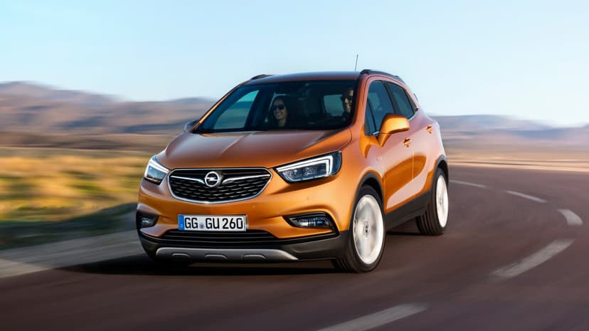 Orange Opel SUV driving fast on a winding desert road with mountains and a clear blue sky in the background.