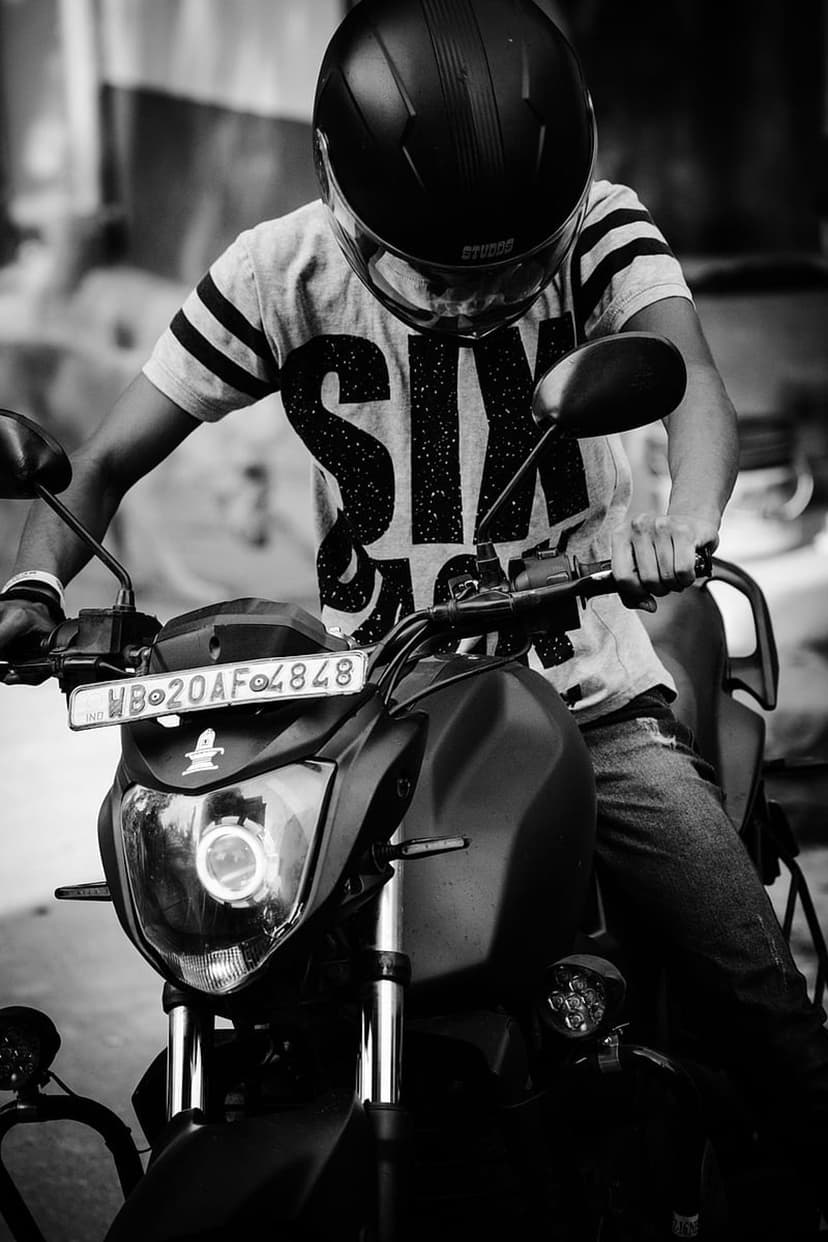 Motorcyclist in a full helmet and six graphic tee sits on a bike with hands gripping the urban handlebars.