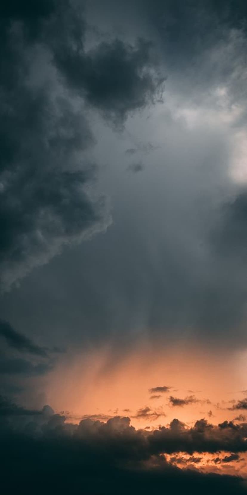 Ominous dark clouds weigh over a brilliant orange and yellow sunset horizon during a powerful weather event.
