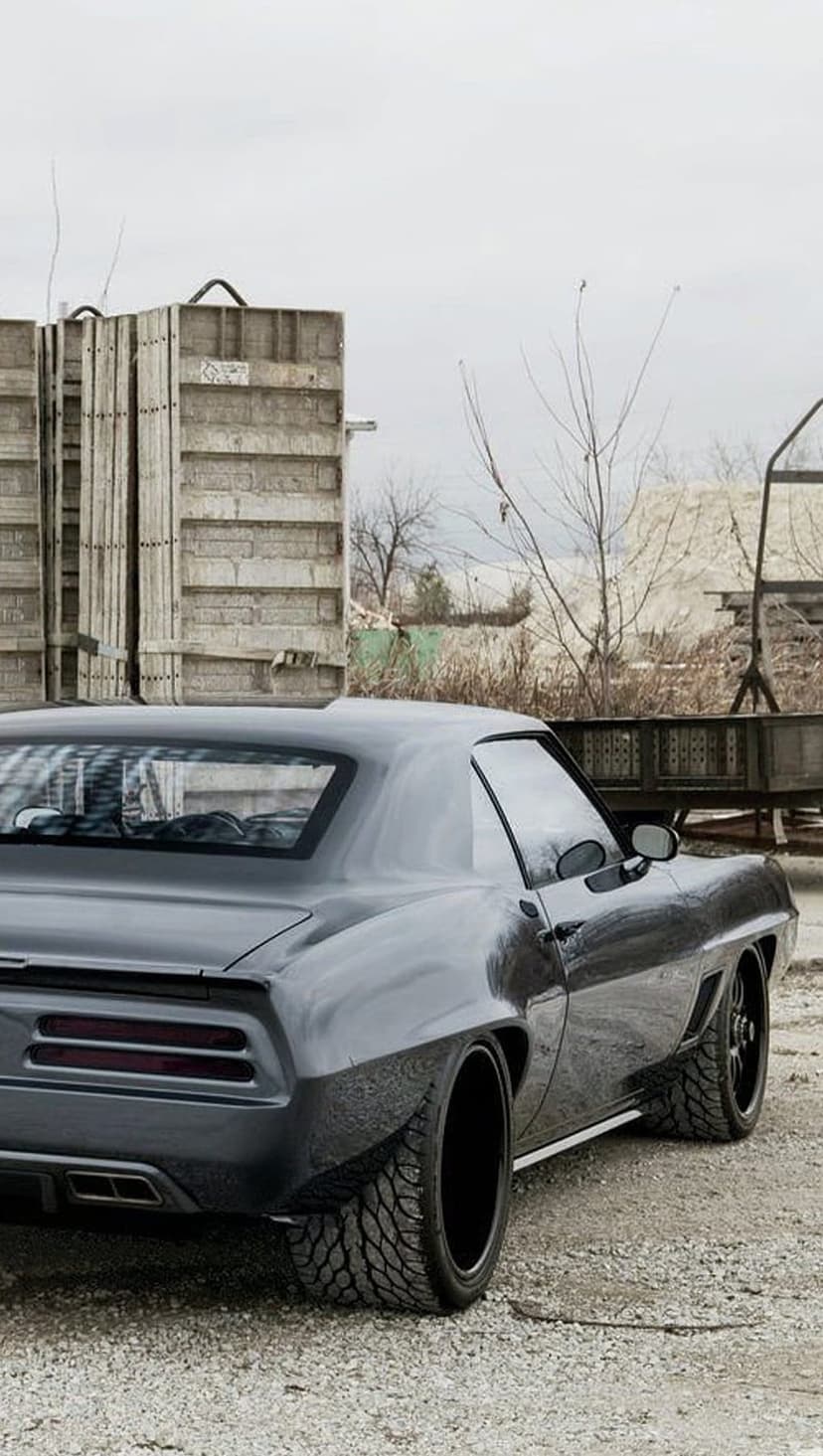 1969 Chevrolet Camaro street rod with a dark gray finish and black wheels parked in an industrial outdoor lot.
