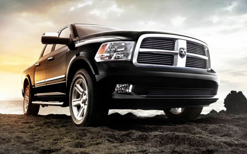 Black Dodge Ram 1500 truck parked on dark volcanic sand with a dramatic sunset sky and chrome grille.