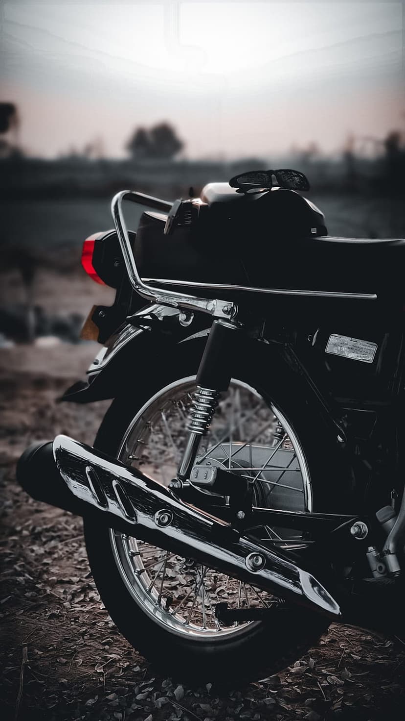 Polished chrome motorcycle exhaust and spoke wheel stand out against a blurred natural landscape at twilight.